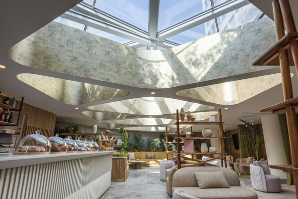 A modern interior with a skylight ceiling, a seating area, and a display of pastries. - Andaz Condesa Mexico City, By Hyatt (Mexico City)