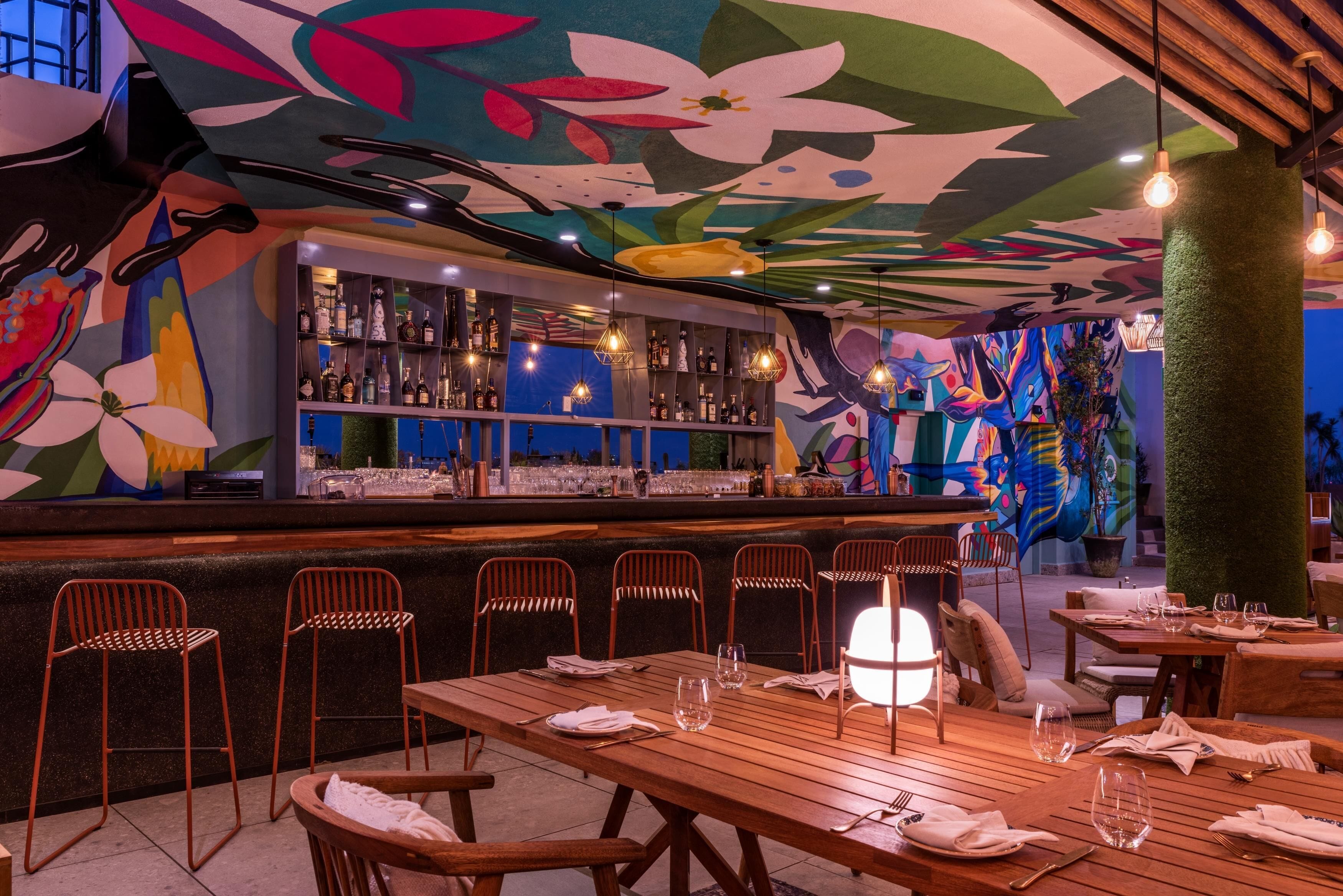 A restaurant with a bar area, wooden tables, and chairs.