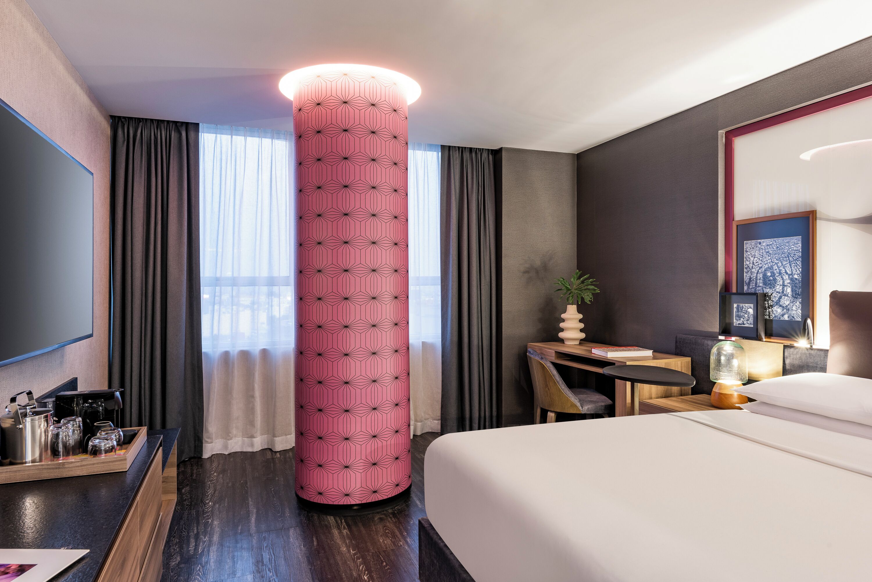 Hotelkamer met een groot bed, een bureau met lamp, een koffiehoek en een grote decoratieve zuil.