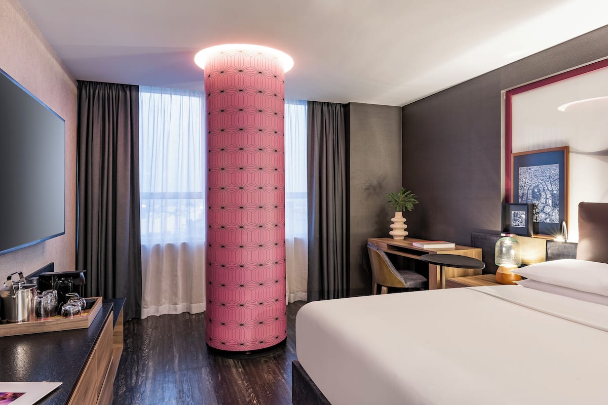 Habitación de hotel con una cama grande, un escritorio con lámpara, una estación de café y un column decorativo de gran tamaño.