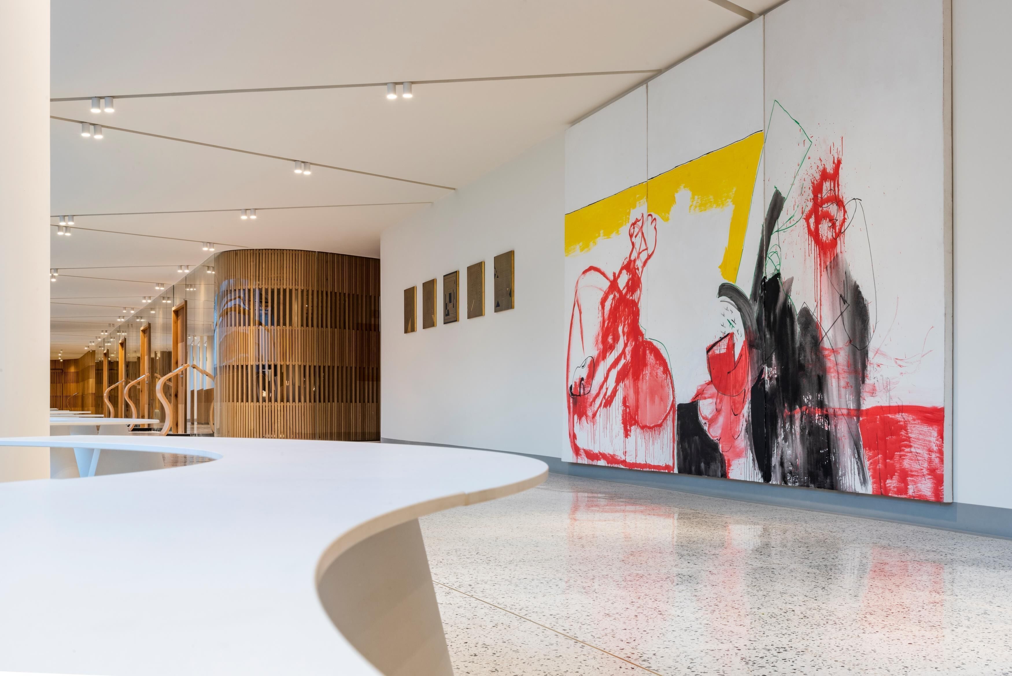 Un intérieur moderne avec un comptoir d’accueil aux lignes courbes, un grand tableau abstrait et un mur à lattes de bois.