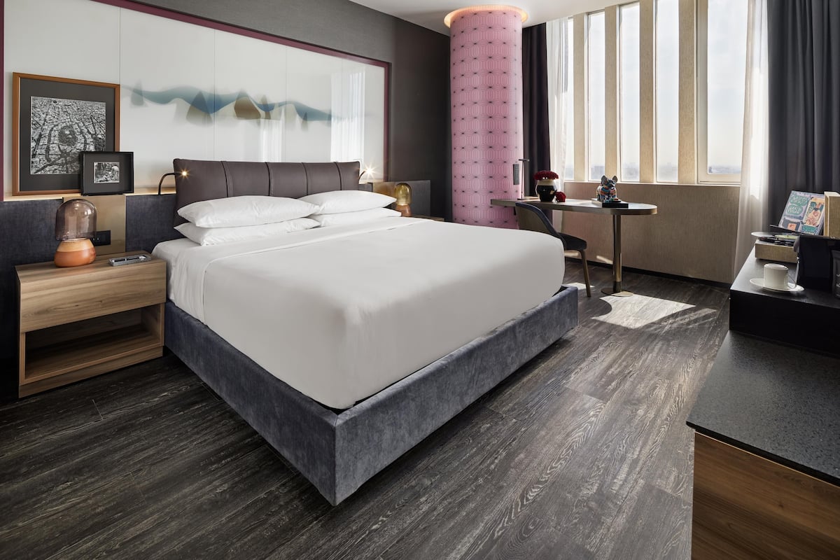 Une chambre d’hôtel moderne, dotée d’un grand lit, d’un bureau et d’une fenêtre avec des rideaux.