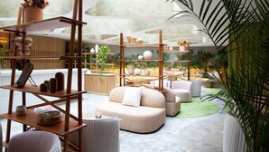 Ein modernes Interieur mit einer zentralen Sitzgruppe, Holzregalen mit Dekoration und verschiedenen Pflanzen.