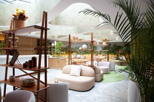 Un interior moderno con una zona de estar central, estanterías de madera con objetos decorativos y una variedad de plantas.
