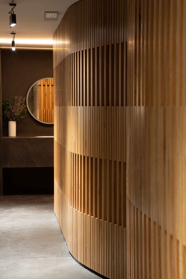 Un área de recepción moderna con un separador de madera curvado, un espejo redondo y una planta en maceta.