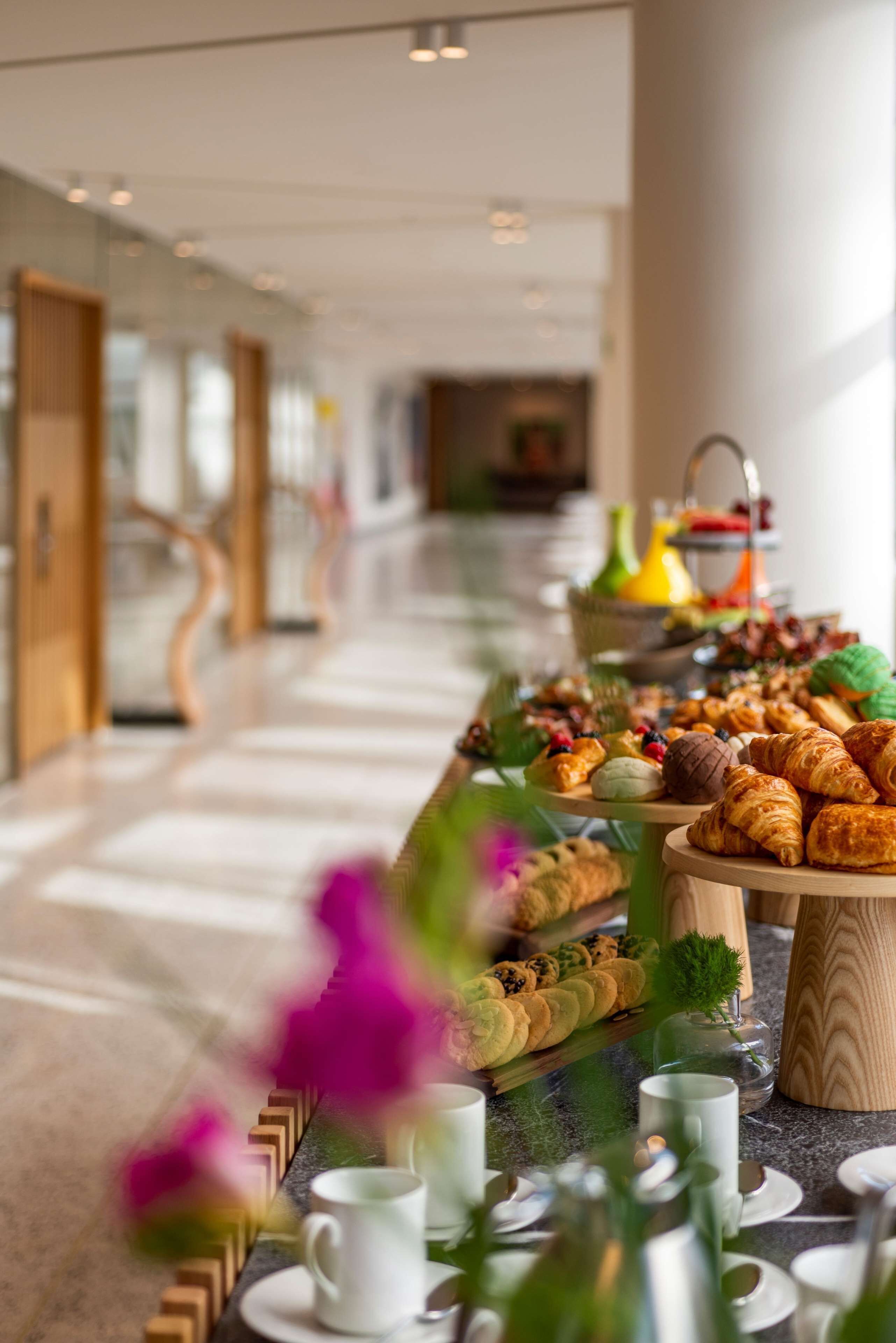 A buffet setup with various pastries and fruits in a modern hotel corridor.