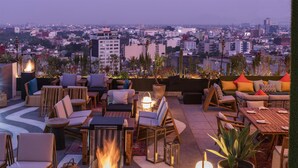 Eine Terrasse im Freien mit Sitzgelegenheiten, einem Feuerbereich und Blick auf die Stadt.