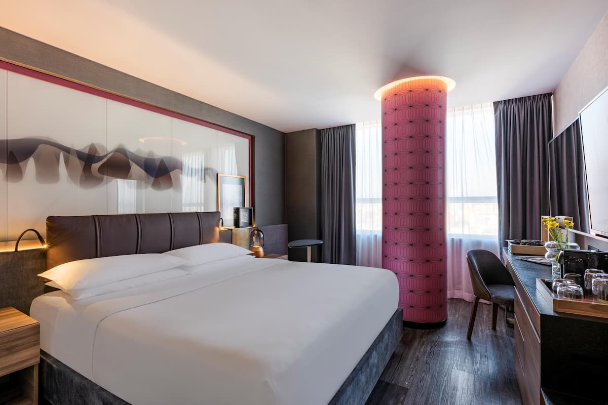 Une chambre d’hôtel avec un grand lit, un bureau avec une chaise, une petite table et un panneau décoratif au mur.