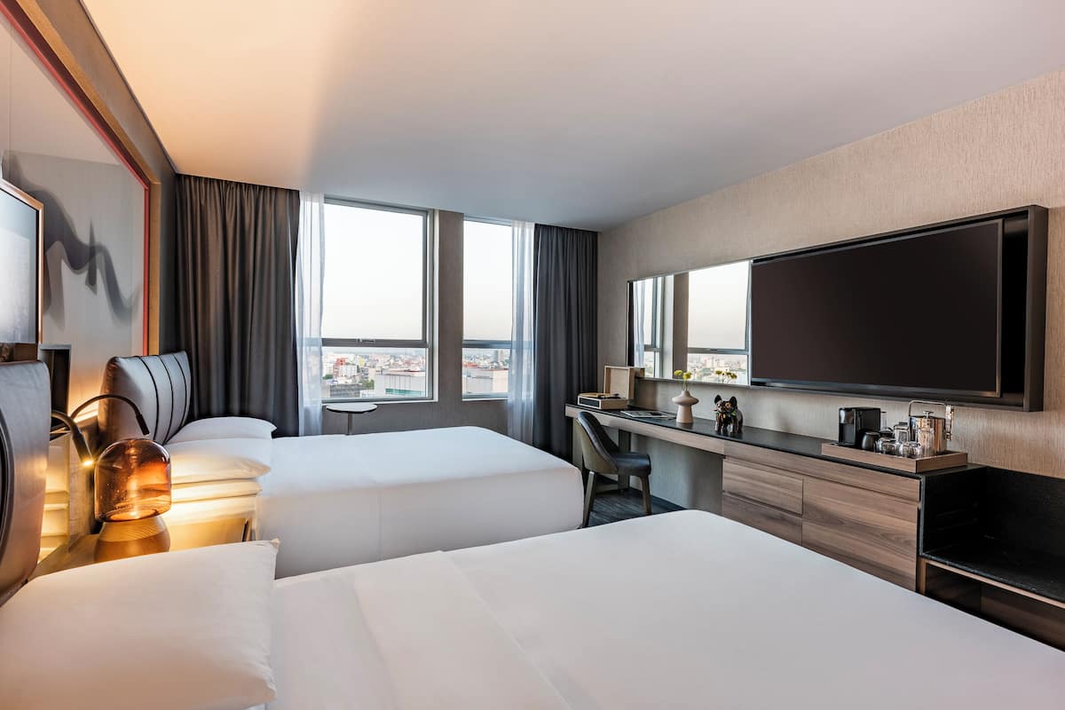 Une chambre d’hôtel avec deux lits, un bureau, une télévision et une vue sur la ville.