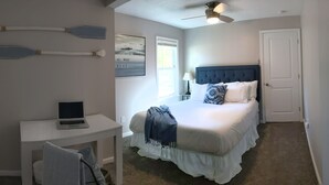 Een slaapkamer met een bed, een bureau met een laptop, een stoel, een plafondventilator en een deur.