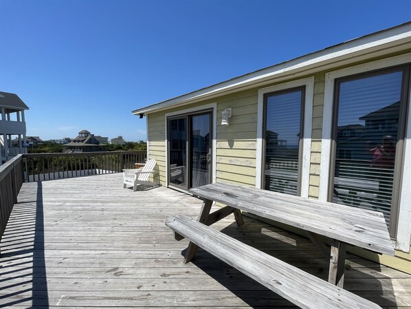 A wooden deck with a bench and chairs, a glass door, and a view of the ocean.