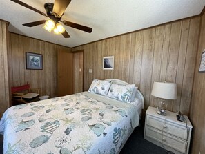 A bedroom with a bed, a nightstand, a chair, a ceiling fan, and wooden walls.