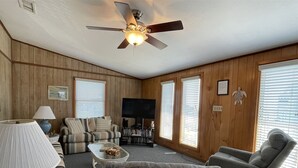 Un salon avec un ventilateur de plafond, un téléviseur, un canapé, une table basse et une cheminée.