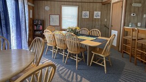 Un coin repas avec une table et des chaises en bois, une bibliothèque et une fenêtre avec des stores.