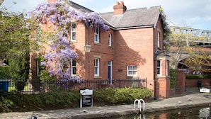 A brick building with purple flowering vines, a canal, and a sign indicating it's a pub. - Lock Keepers Cottage - Detached House in the City (Manchester)