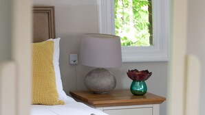 A neatly made bed with white linens, a yellow pillow, a lamp on a wooden nightstand, and a vase with red flowers. - Lock Keepers Cottage - Detached House in the City (Manchester)