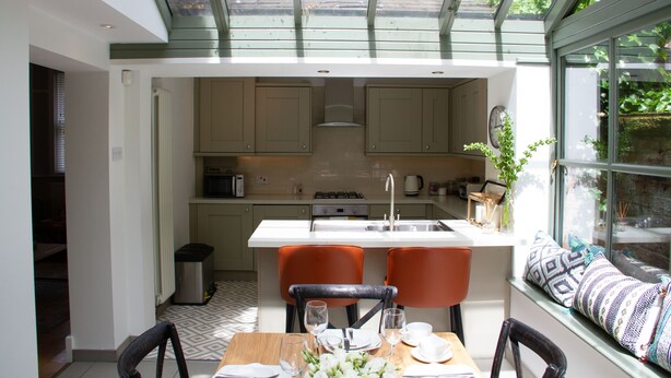 A modern kitchen with a central island, two orange chairs, and a dining table set for four. - Lock Keepers Cottage - Detached House in the City (Manchester)