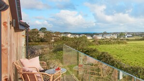 A balcony with wicker chairs and a table, overlooking a green landscape and houses. - Birch House, situated just outside of the beautiful lively village of St Agnes and only 1.5 miles fr (St Agnes)