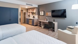 Una habitación de hotel con dos camas, un kitchenette, un escritorio, una silla y un televisor.