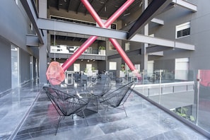 A modern indoor space with a glass ceiling, metal railings, and a seating area with chairs.