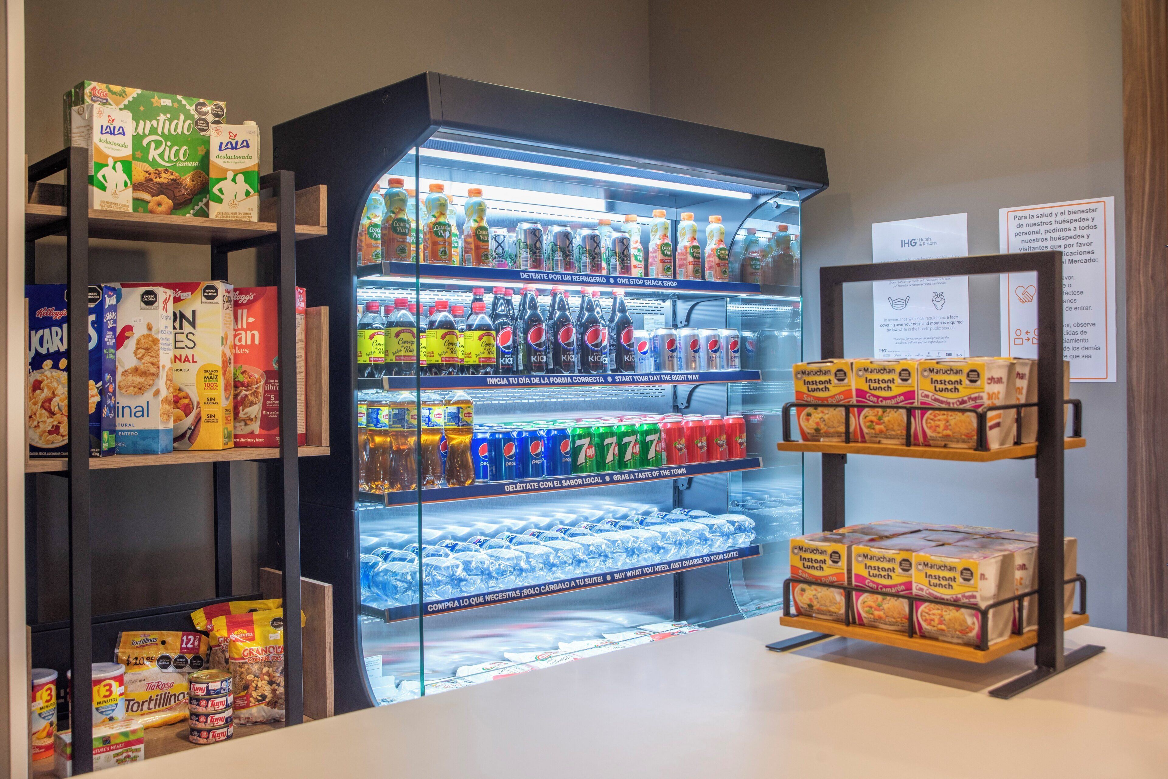 Mostrador refrigerado con bebidas variadas y barra de aperitivos con productos alimenticios preparados.
