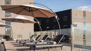 Sillas de lounge al aire libre con sombrillas, una piscina y un edificio con la leyenda "Candlewood Suites".