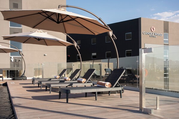Outdoor lounge chairs with umbrellas, a pool, and a building labeled "Candlewood Suites".
