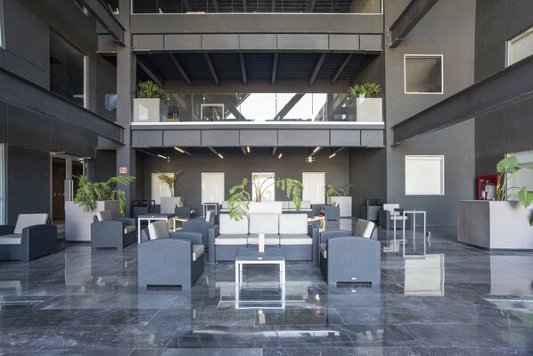 A spacious lobby with a modern design, featuring a central seating area with sofas and chairs, a high ceiling with exposed beams, and potted plants. - Candlewood Suites Guadalajara Galerias by IHG (Zapopan)