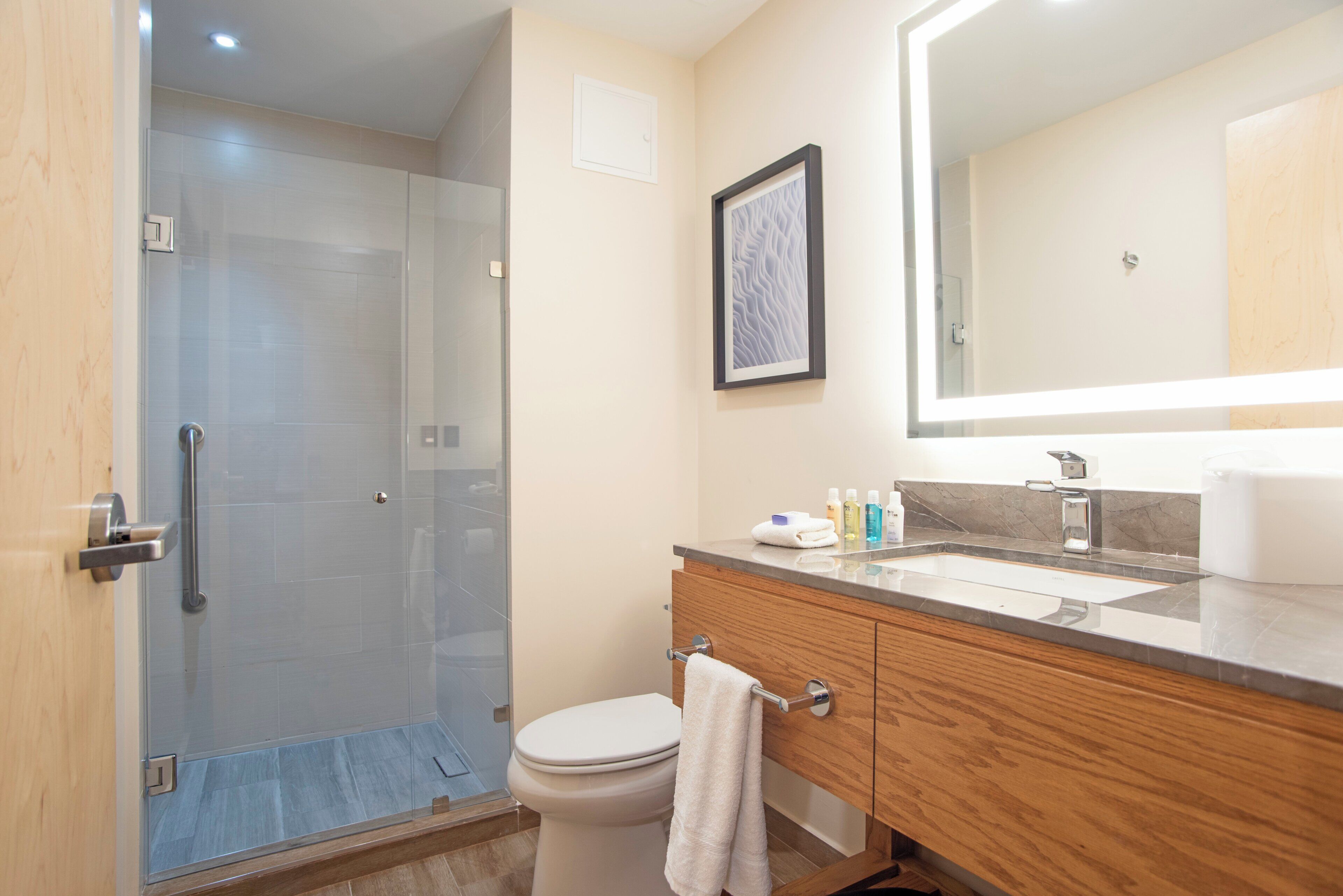 Une salle de bain moderne avec une douche à parois de verre, des toilettes, un meuble-lavabo avec un miroir et des articles de toilette.