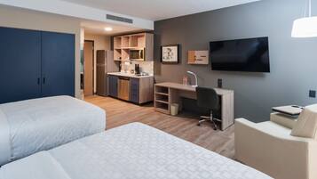 A hotel room with two beds, a kitchenette, a desk, and a TV.