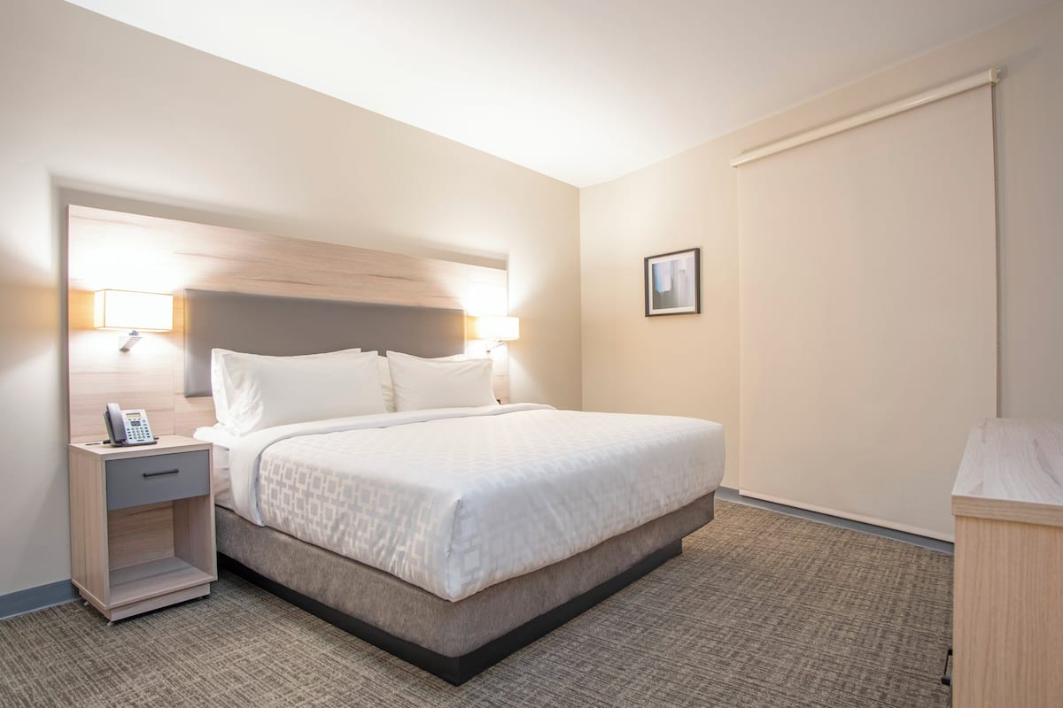 Ein Hotelzimmer mit einem Bett, einem Nachttisch, einer Lampe und einem kleinen Regal mit einem Telefon.