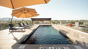Una piscina en la azotea con sillones de descanso y sombrillas, un flotador salvavidas y un letrero que indica que no está permitido bucear.