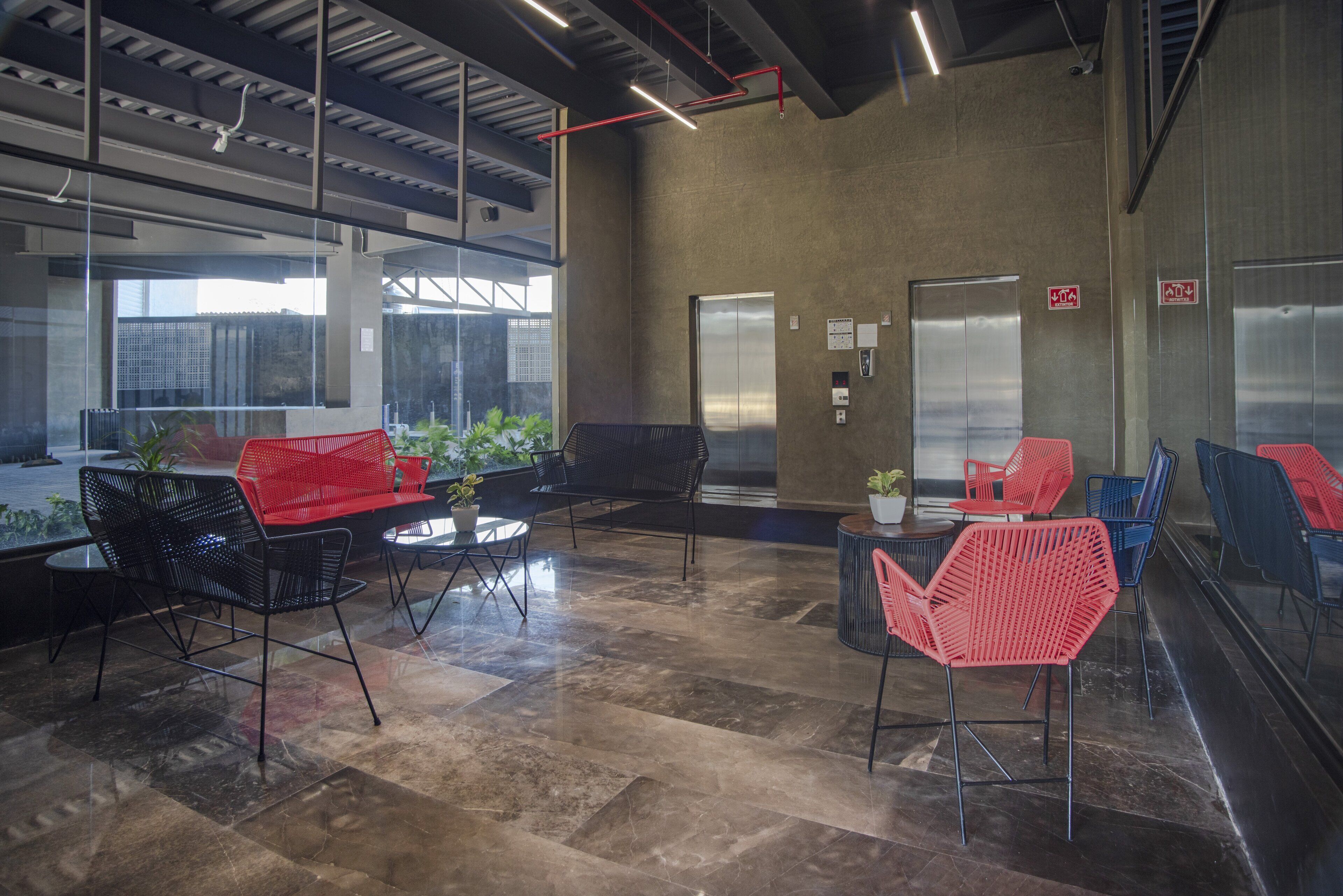 Un espace intérieur moderne offrant différents types de sièges, notamment des chaises noires et rouges, ainsi qu'une cloison en verre.