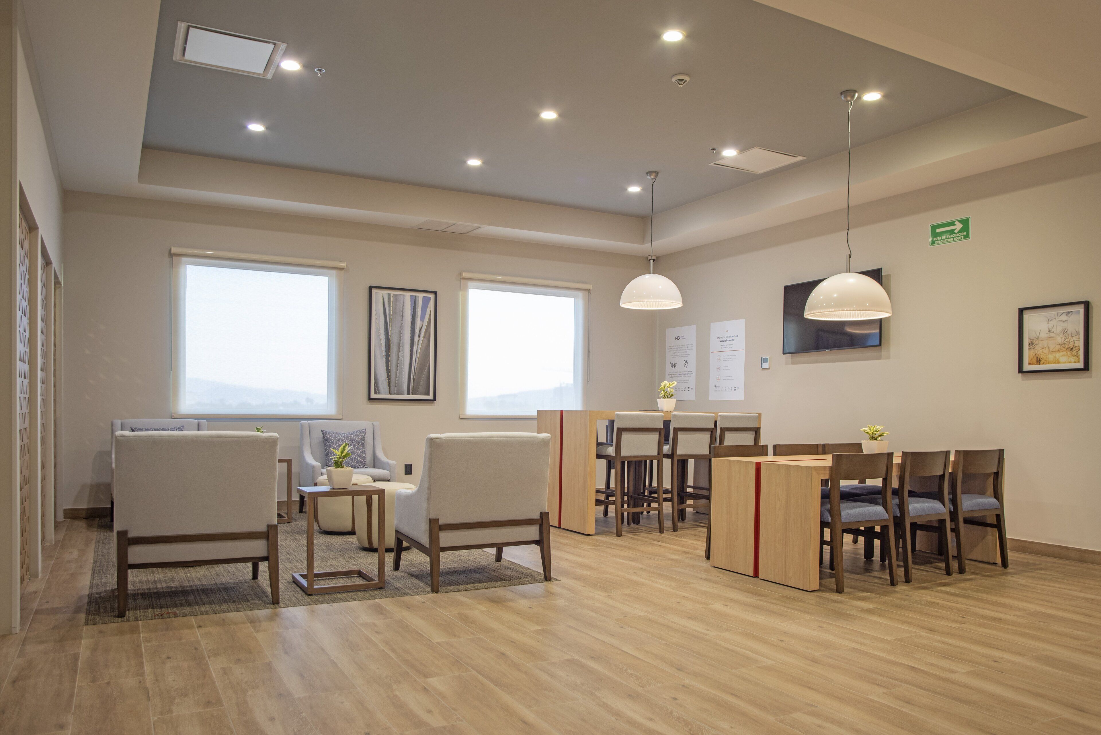 A spacious room with a wooden floor, multiple seating areas including a sofa and chairs, a small table with a plant, and a ceiling with recessed lighting.