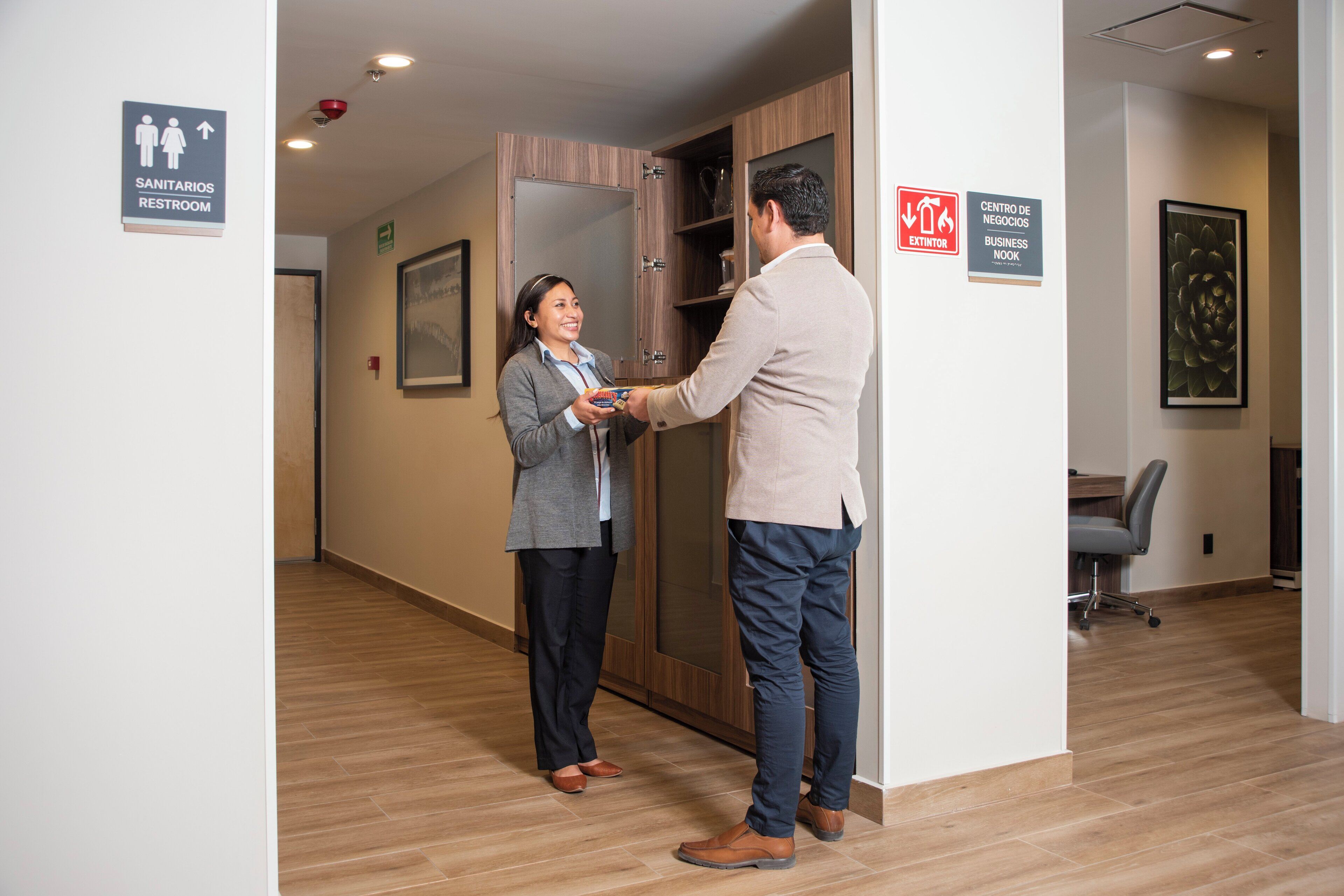 A hallway with a restroom sign, a business center sign, and a framed artwork on the wall.