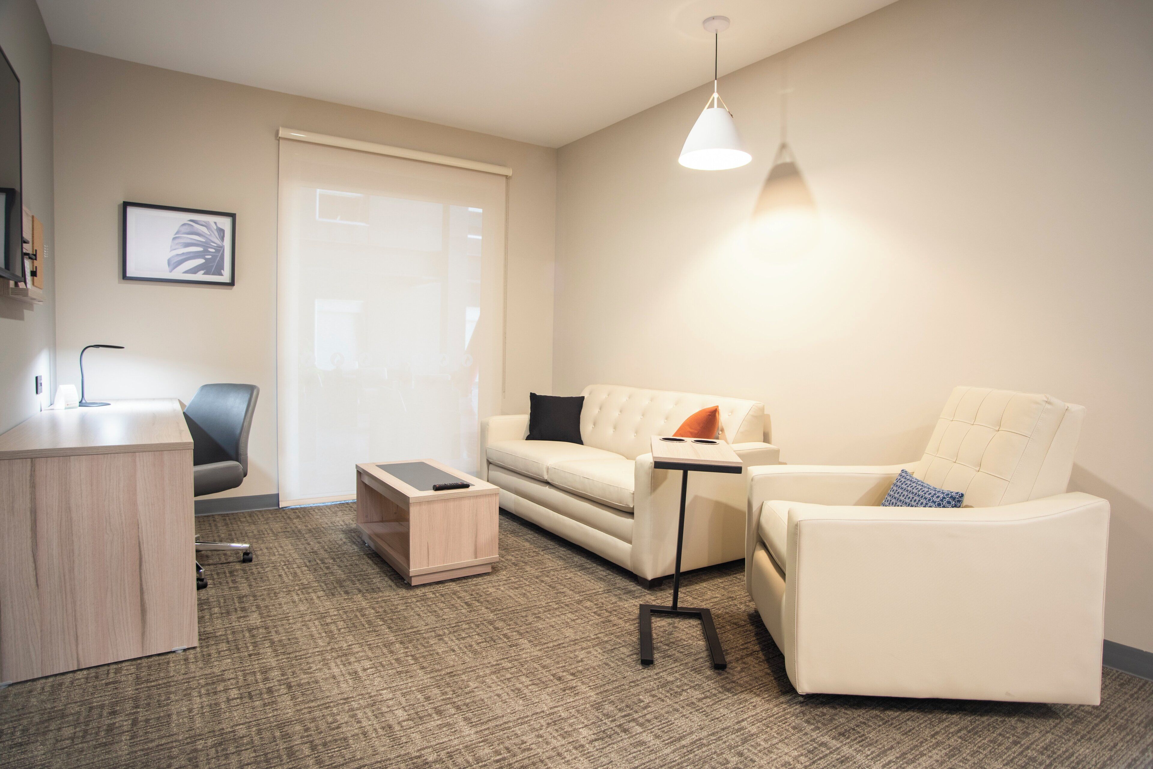 A modern living room with a sofa, armchair, coffee table, and a desk with a lamp.