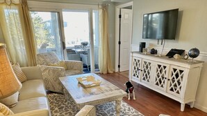 A living room with a sofa, patterned armchairs, a coffee table, a TV, and a cabinet with decorative items. - Direct Ocean Views from your bed & screened-in deck.Pet friendly! 2br 2bth (Dewey Beach)