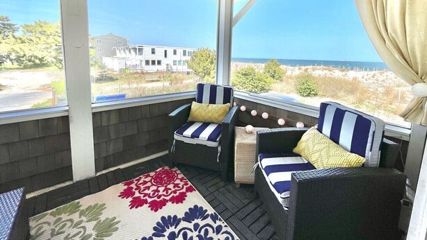 A covered porch with wicker furniture, a view of the beach, and a house in the background. - Direct Ocean Views from your bed & screened-in deck.Pet friendly! 2br 2bth (Dewey Beach)