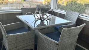 A dining area with wicker chairs and a glass table, overlooking a residential area with houses and trees. - Direct Ocean Views from your bed & screened-in deck.Pet friendly! 2br 2bth (Dewey Beach)