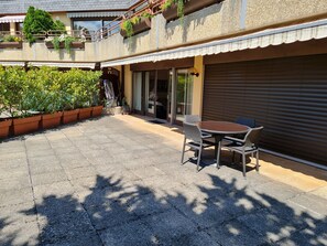 A patio with a table and chairs, surrounded by potted plants and a covered area with a sliding door. - Paradise lake view Apartment (Veytaux)