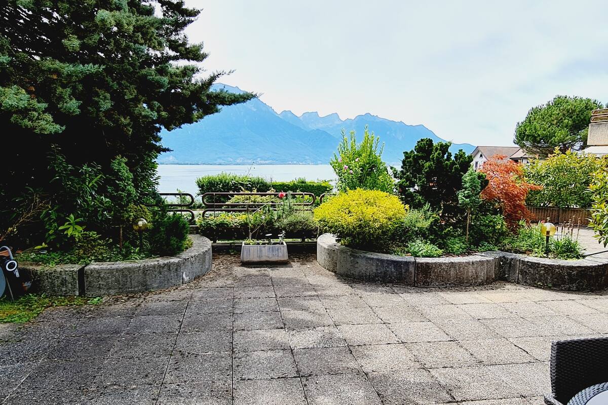 Un patio empedrado con jardineras y vistas a un lago y montañas.