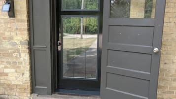 Une porte brun foncé avec un panneau de verre, un paillasson sur lequel est écrit « Soyez les bienvenus », et un mur de briques.