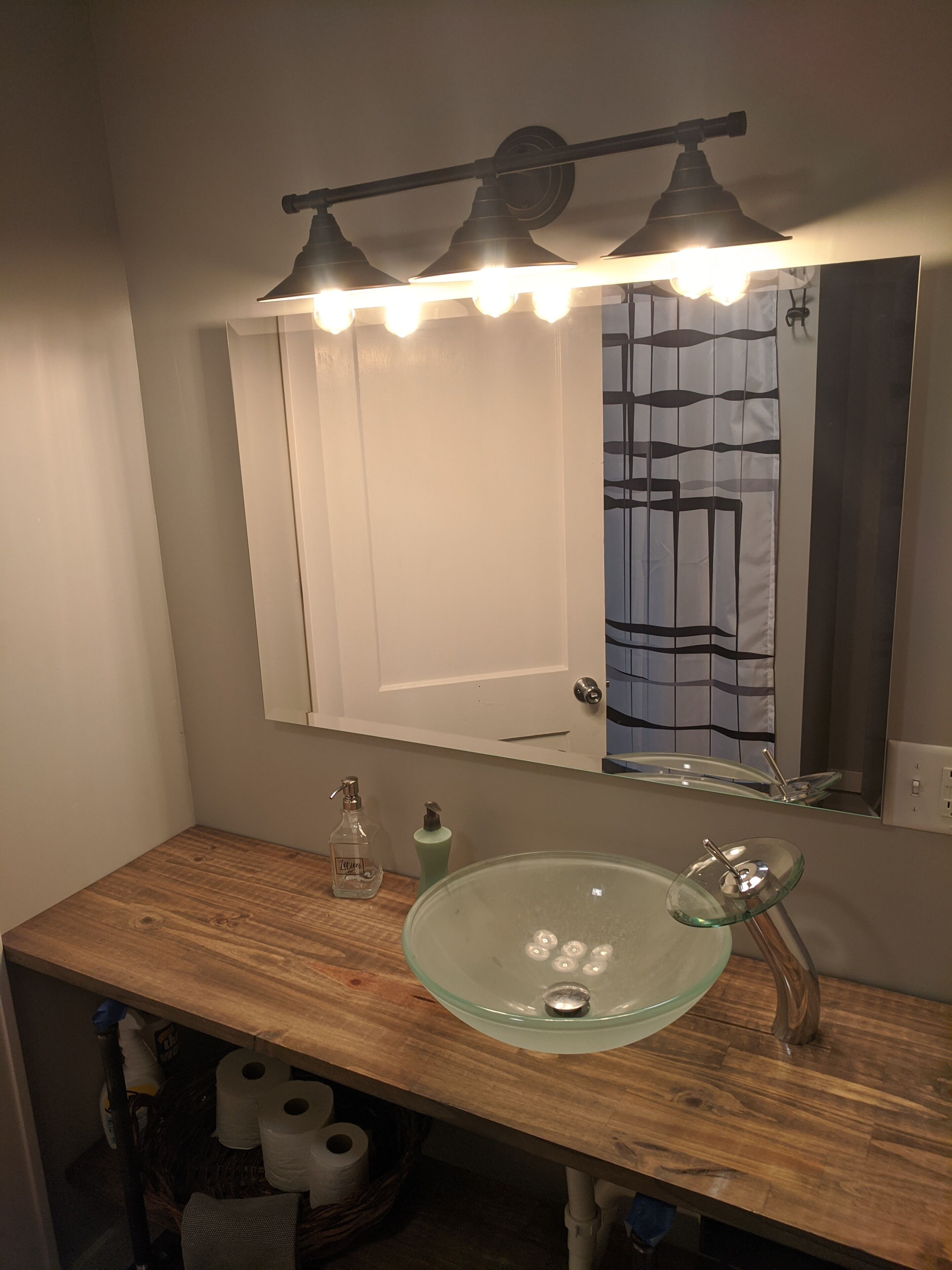 Une salle de bain avec un meuble-lavabo en bois, un vasque en verre et un miroir surmonté d’un luminaire.