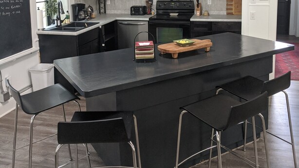 A modern kitchen with dark cabinetry, a central island with stools, and a blackboard with writing. - Restored school house turned creative flex space (Perham)