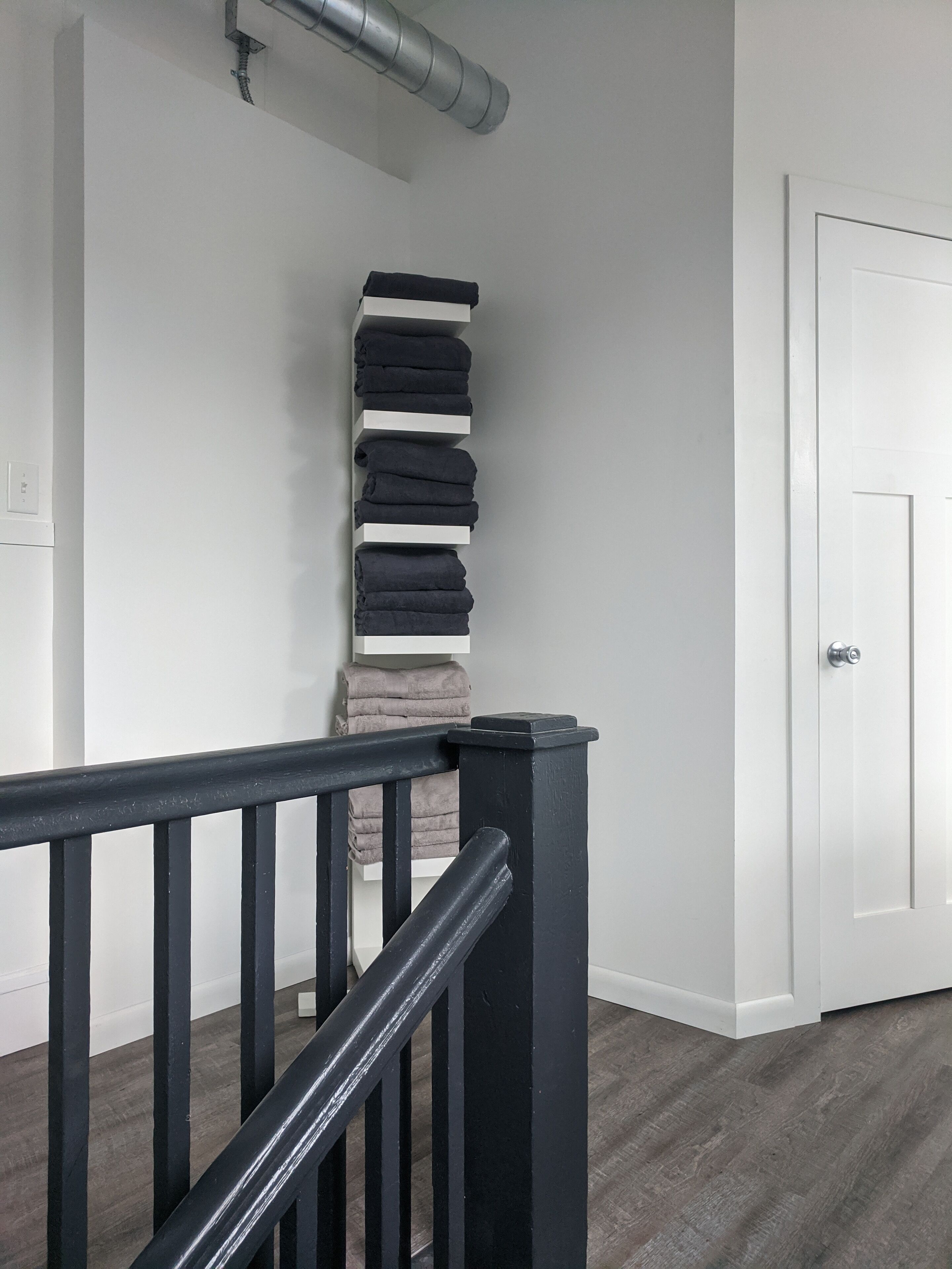 Un escalier avec une rampe noire mène à un palier. Une porte blanche est visible sur la droite.