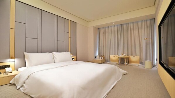 Habitación de hotel moderna con una cama grande, mesitas de noche, un escritorio y un amplio ventanal con cortinas.