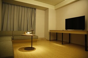 A modern living room with a sofa, a small round table with a tray of items, a television on a stand, and a wooden floor. - Ji Hotel (Shanghai)