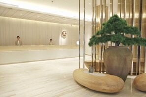 Un área de recepción de diseño moderno, con mostrador de recepción, un logotipo en la pared y una planta grande en maceta.