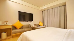 Habitación de hotel con cama, sofá, televisión, una mesita con bandeja y ventana con cortinas.