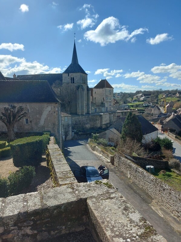 A historic stone building with a prominent tower, surrounded by a cobblestone pathway and lush greenery.